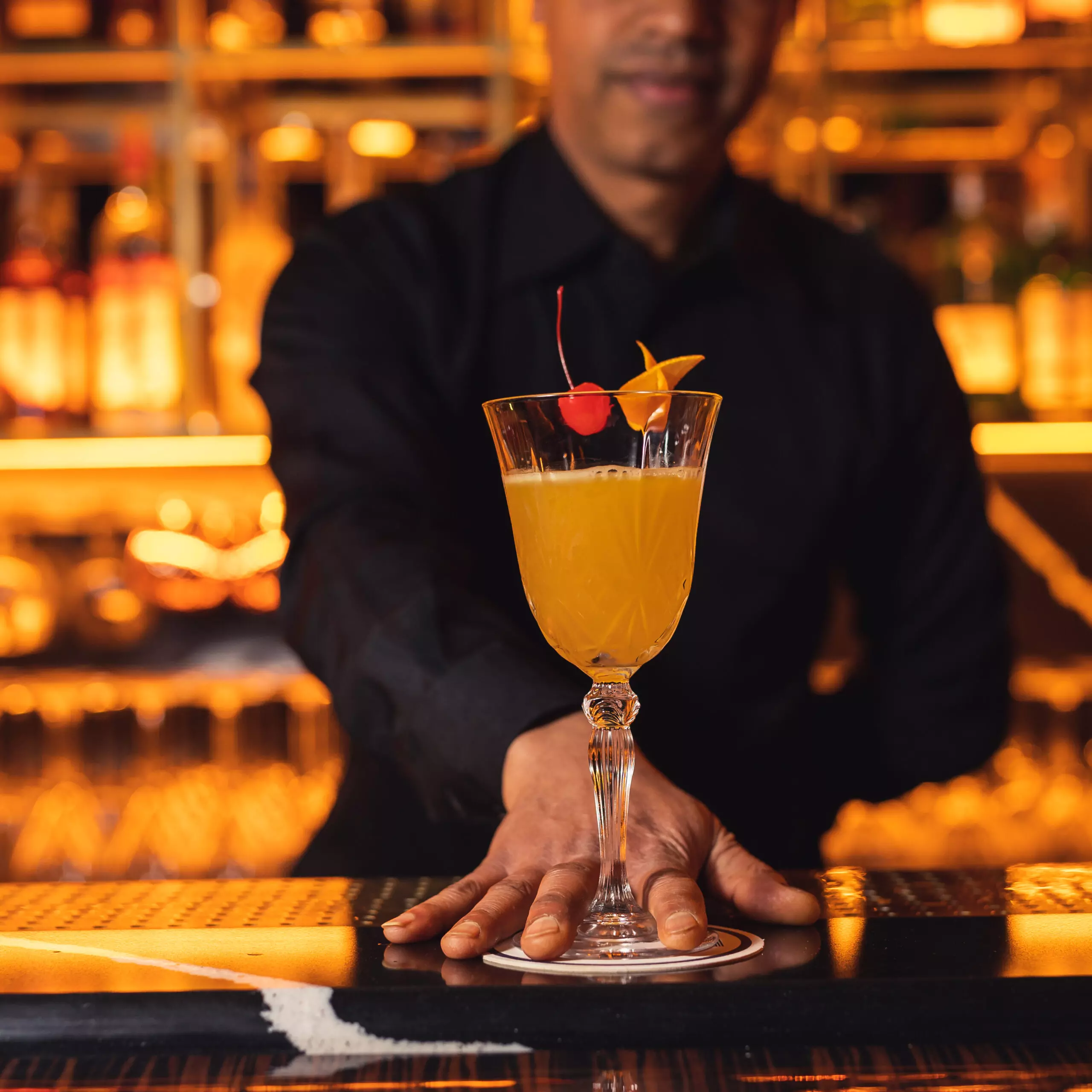 Un delizioso cocktail per l'aperitivo, servito in un bicchiere di vetro con una fetta di arancia fresca e una ciliegia come decorazione.